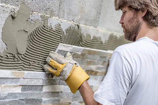 Person bringt Natursteine an Wand an